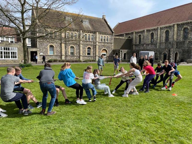Ein große Gruppe von Kindern spielen Tauziehen draußen in einem großen Innenhof einer antiken Kirche  bei den Sprachreisen Großbritannien