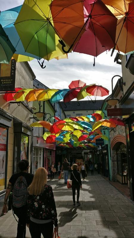 In einer Gasse schweben viele bunte Regenschirme zwischen den Häusern