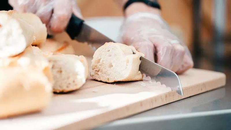 Ein Koch schneidet im Surf-Camp Südfrankreich ein Baguette klein