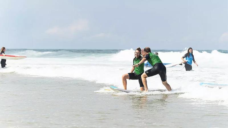 Ein Surftrainer gibt einer Jugendlichen im Surf-Camp Frankreich ein High Five beim Surfen