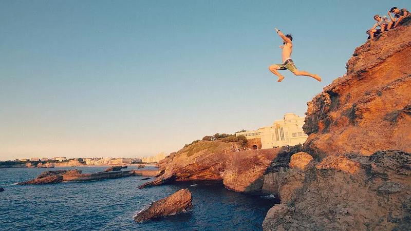 Ein Junge springt von einer Klippe ins Wasser im Surf-Camp Frankreich