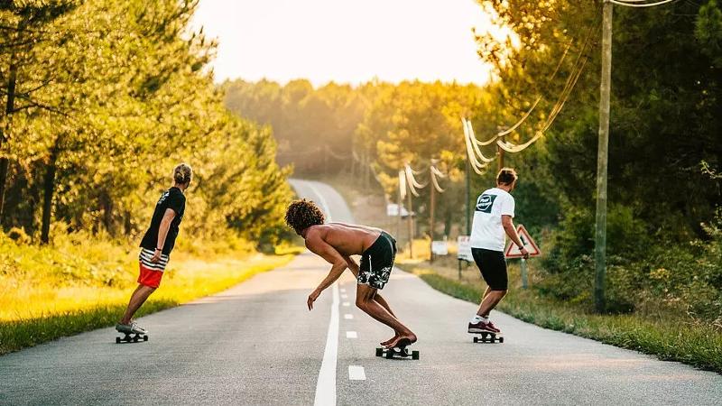 Im Surf-Camp Frankreich fahren 3 Jungs mit ihrem Longboard eine Straße entlang