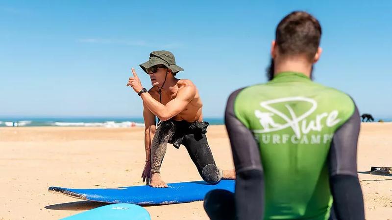 Der Surflehrer vom Surf-Camp Frankreich erklärt den Teilnehmern einige Basics am Strand