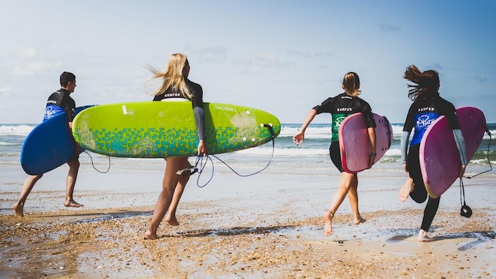 Gruppe rennt in der Ferienfreizeit Jugendliche mit Surfbrettern am Strand entlang
