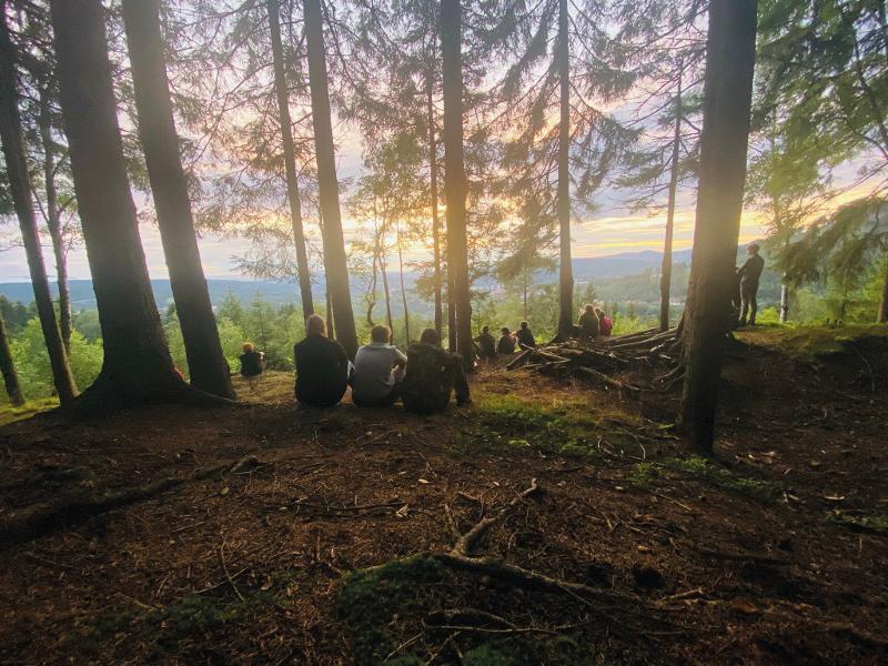 Teilnehmer der Ferienbetreuung sitzen im Wald und genießen den Ausblick