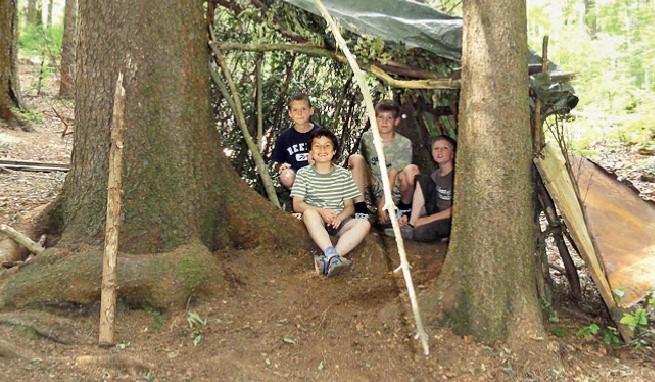 Vier Jungs sitzen auf Kinderreise im selbstgebauten Zelt