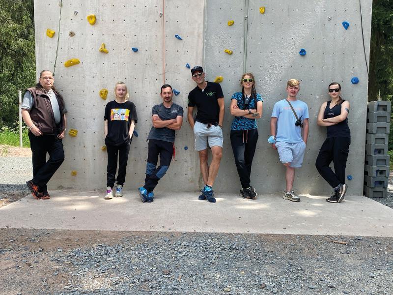 Die Betreuer stehen gemeinsam im Outdoorcamp vor einer Kletterwand