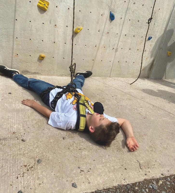 Im Outdoor Feriencamp liegt ein Junge vor der Kletterwand