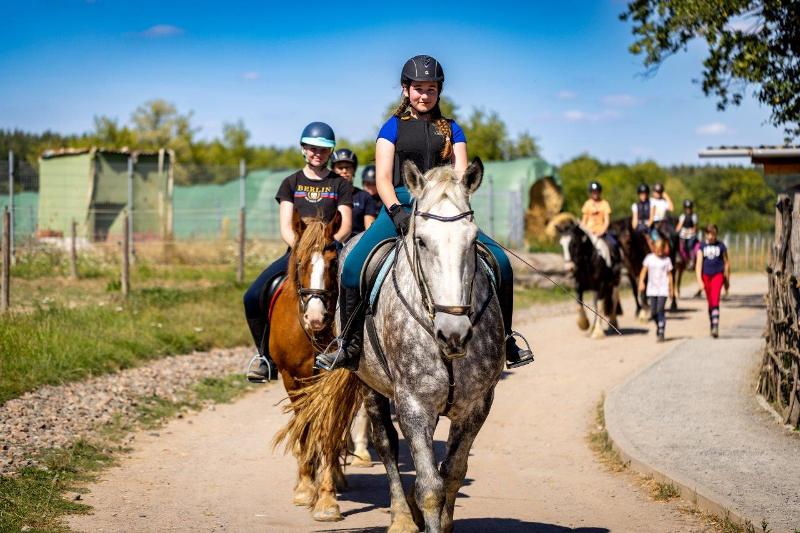 Einige Kinder sitzen jeweils auf ihren Pferden und sie machen zusammen einen Ausritt bei den Osterferien in der Jugendherberge 