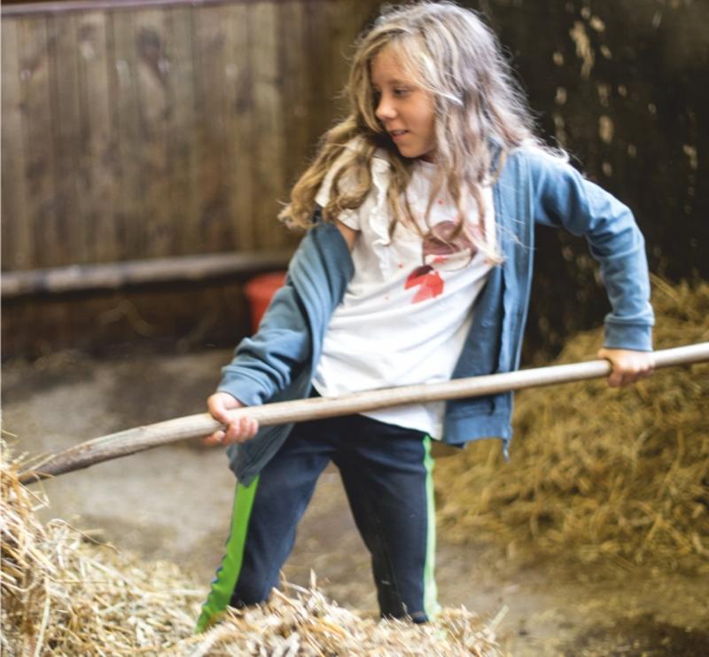 Ein Mädchen mistet im Ponycamp eine Box aus