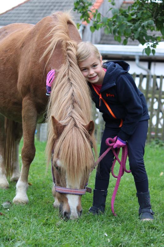 Ein Mädchen kuschelt in einem Ponycamp mit ihrem Pferd