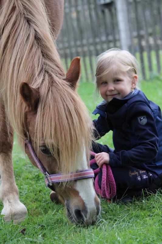 Ein kleines Mädchen sitzt bei einem Ponycamp auf einer Wiese