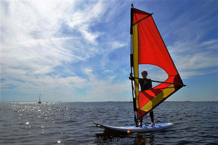 Ein Junge verbringt den Jugendurlaub Deutschland mit Windsurfen auf dem Meer bei gleißendem Sonnenlicht