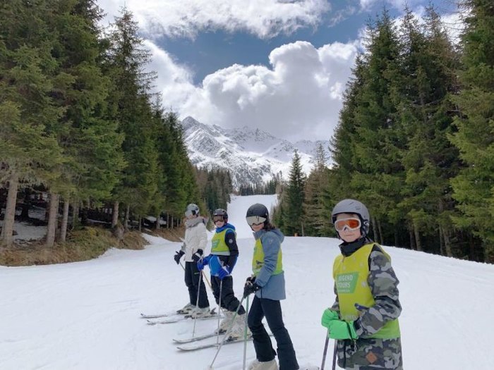 4 Kinder verbringen ihre Jugendreise damit, auf der Piste mit den Skiern angeschnallt in einem Waldgebiet die Abfahrt zu genießen