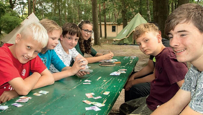 Kinder vom Beetzee Ferienlager spielen an einem Tisch im Wald Karten