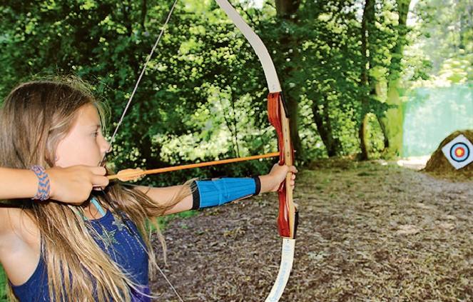 Mädchen zielt mit Pfeil und Bogen auf Zielscheibe im Ferienlager in Gadow