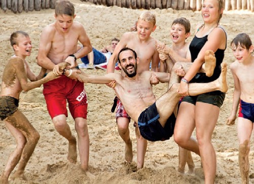 Kinder tragen einen Betreuer lachend über den Sandstrand