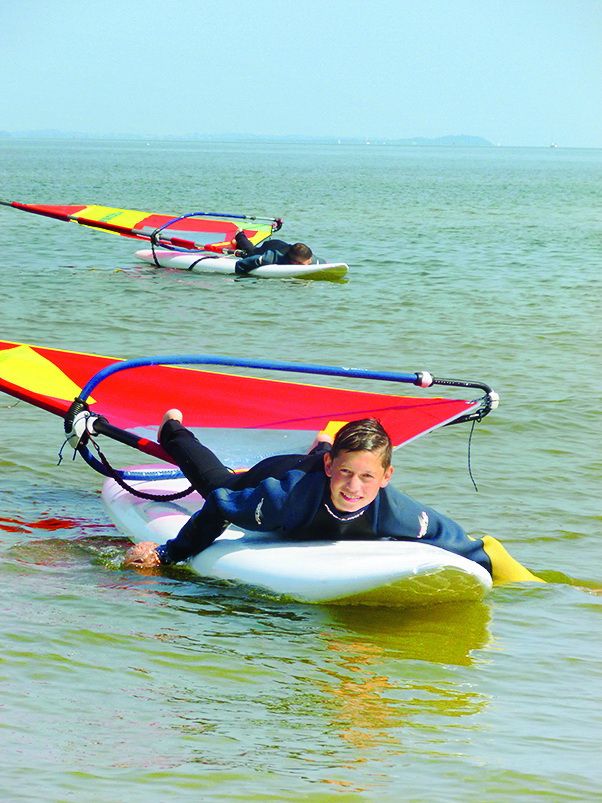 Ein Junge liegt im Windsurfcamp auf dem Brett.