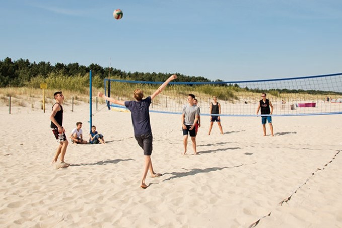 Eine Gruppe an Jugendlichen spielt auf ihrer billigen Jugendreise am Strand Volleyball.