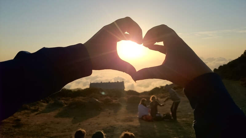 Jemand zeigt ein Herz mit den Händen in die Sonne im Feriencamp für Schüler