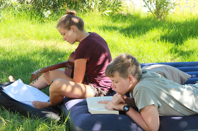 Kinder lesen und spielen Gitarre auf Wiese auf Ferienfreizeit Korsika