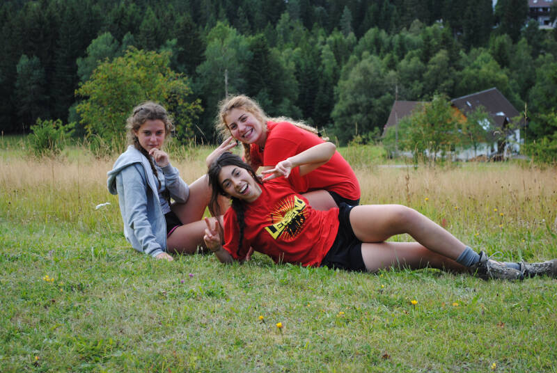 Drei Mädchen des Jugendcamps Attersee liegen auf einer Wiese vor einem bergigen, natürlichem Hintergrund im Sommer