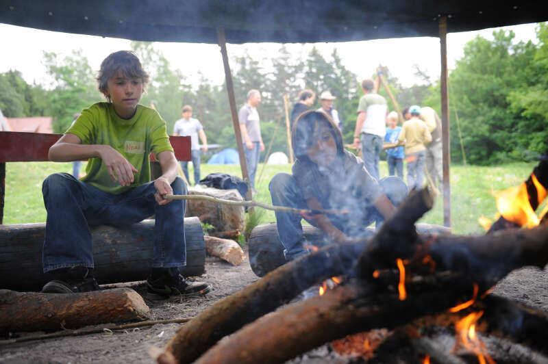 Eine Gruppe Kinder sitzen in ihrer Ferienbetreuung Brandenburg am Lagerfeuer