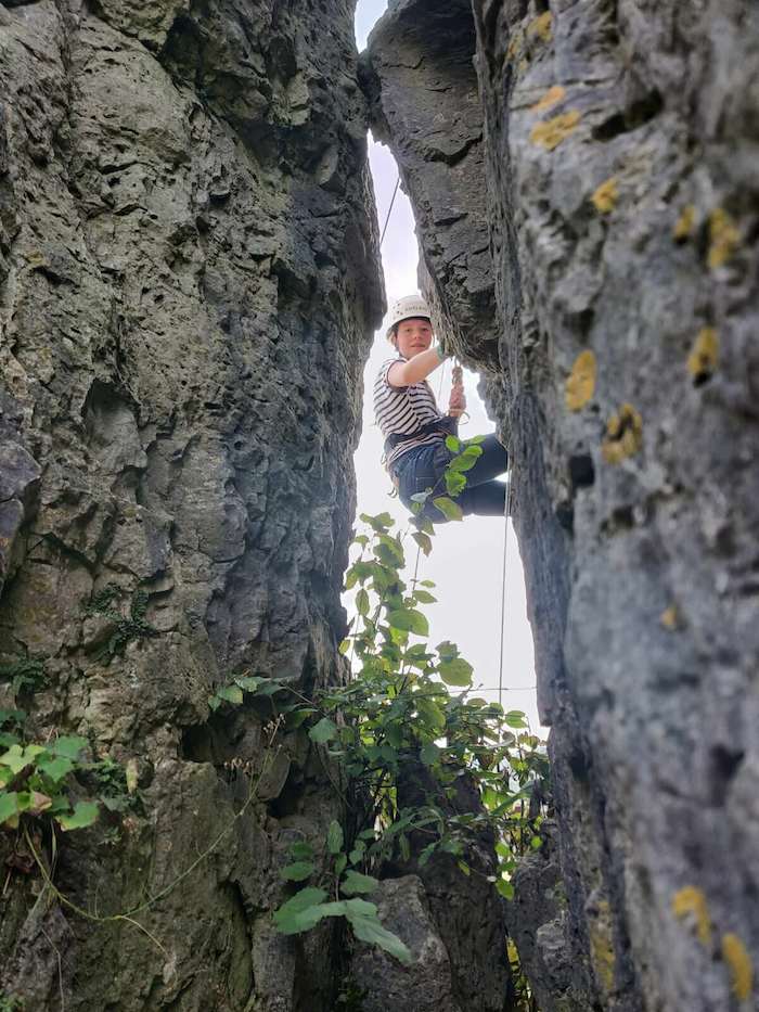 Kletterender Jugendlicher zwischen zwei Felsen in der Ferienfreizeit Jugendliche