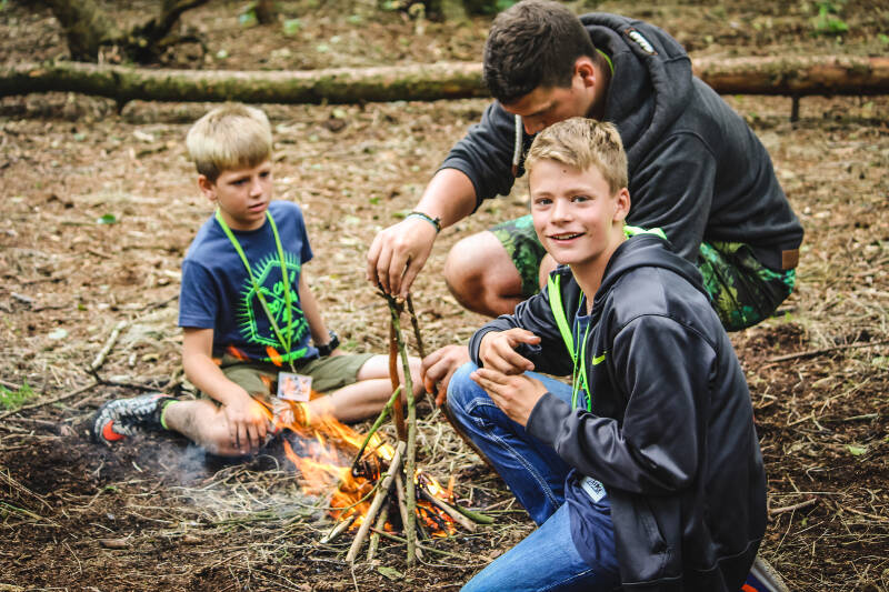 Kinder eines Naturcamps für Kinder sitzen im Wald und machen ein Feuer