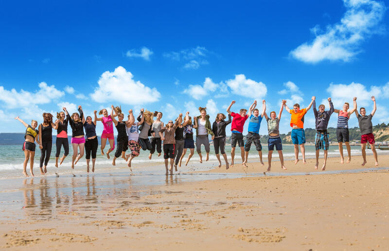Eine große Gruppe von Jugendlichen springt am Strand in einer Reihe nebeneinander in die Höhe