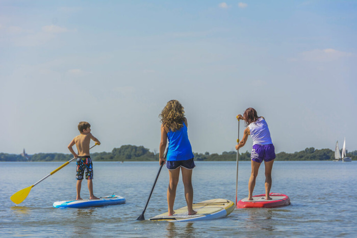 Drei Kinder der Jugendherberge Englischcamps sind am SUP boarden auf einem See