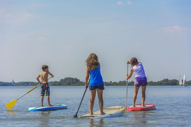 Drei Kinder fahren mit einem Standup Paddling Board über einen See bei ihrer Englisch-Sprachreise in Deutschland.
