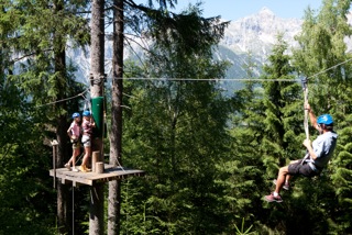 Drei Kinder sind zwischen den Baumwipfeln am Klettern in einem Kletterpark im Ferienlager Waadt.