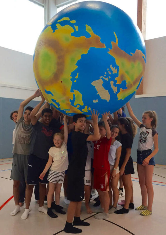 Teilnehmer eines Kindersprachkurses halten einen großen Erd-Ball