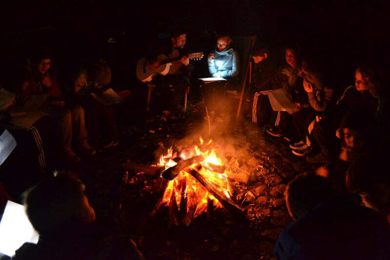 Kinder sitzen und singen am Lagerfeuer auf der Ferienfreizeit in Nordrhein-Westfalen
