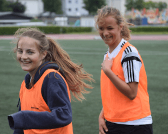 Zwei Freundinnen lächeln im Fußballcamp in die Kamera.