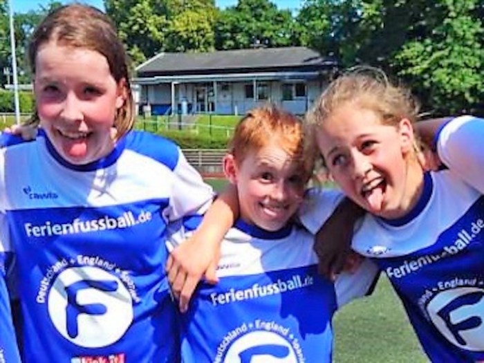Drei Mädchen grinsen im Fußballcamp in die Kamera und ziehen lustige Grimassen.