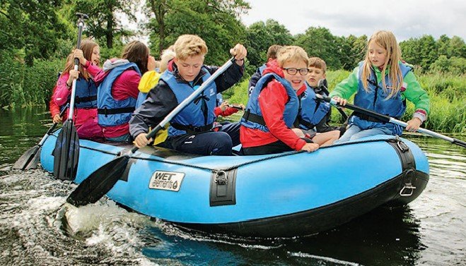 Kinder sitzen im Schlauchboot und paddeln über den See