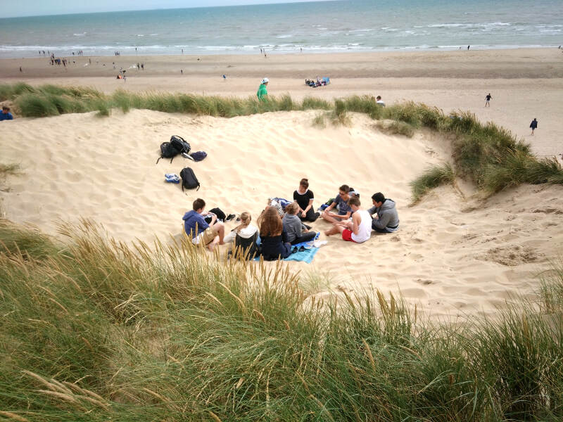 Jugendliche sitzen zwischen bewachsenen Dünen am Sandstrand von Hastings