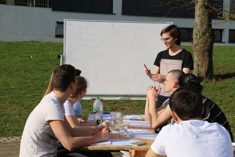 Jugendliche sitzen draußen an einem Tisch und hören jemandem zu