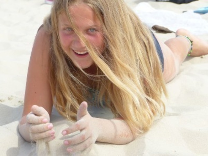Mädchen liegt lachend im Sand im Ferienlager in Mecklenburg-Vorpommern