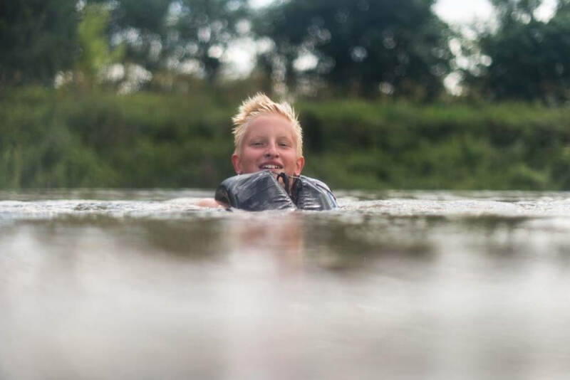 Junge schwimmt mit Rettungsweste im Fluss im Ferienlager