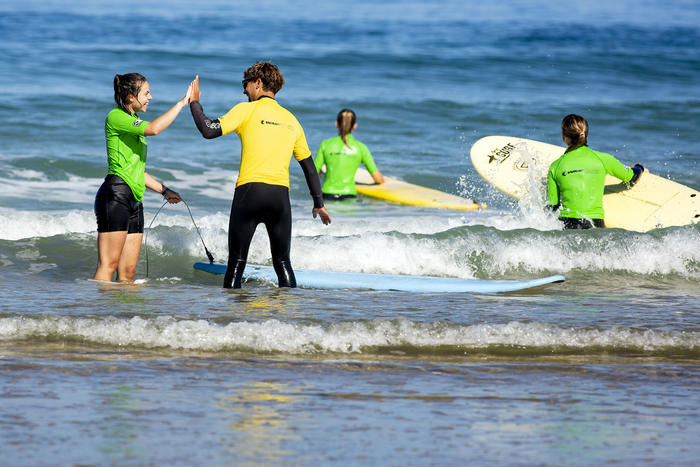 Jugendliche stehen im Wasser und machen High five im Surfcamp in Südfrankreich