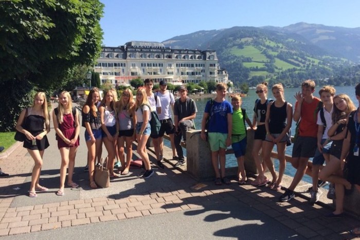 Jugendliche stehen am Ufer des Zeller See bei strahlendem Sonnenschein mit den Bergen des Salzburger Lands im Hintergrund