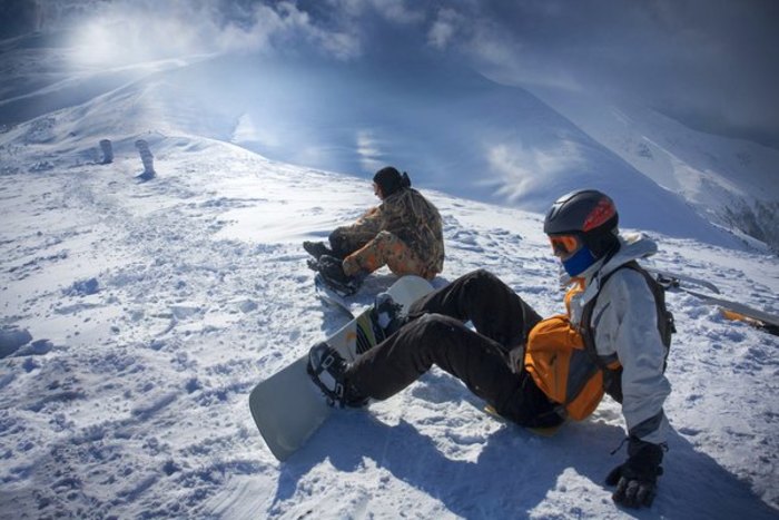 Zwei Jugendliche sitzen auf einem Berghang im Salzburger Alpenland mit festgeschnallten Snowboards im Schnee