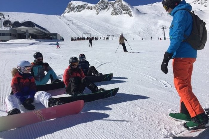Kinder sitzen an einer Pistenabfahrt im Salzburger Alpenland mit festgeschnallten Snowboards im Schnee