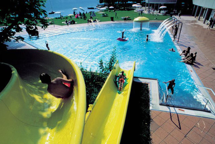 Feriengäste auf der Wasserrutsche im Freibad am Ufer des Zeller Sees mit dem Salzburger Alpenland im Hintergrund