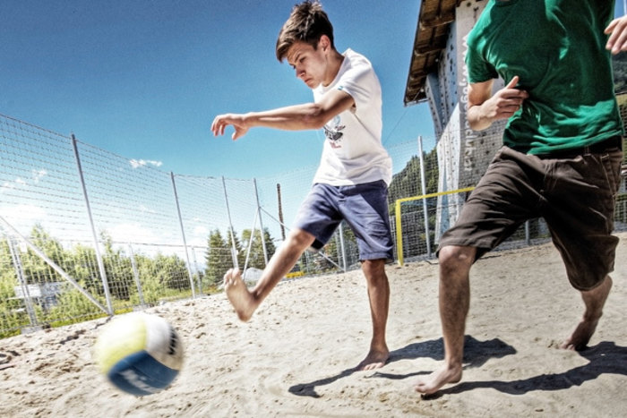 Kinder spielen Fußball auf einem Sandplatz im Außenbereich des Jugendhotels Club Kitzsteinhorn in Zell am See