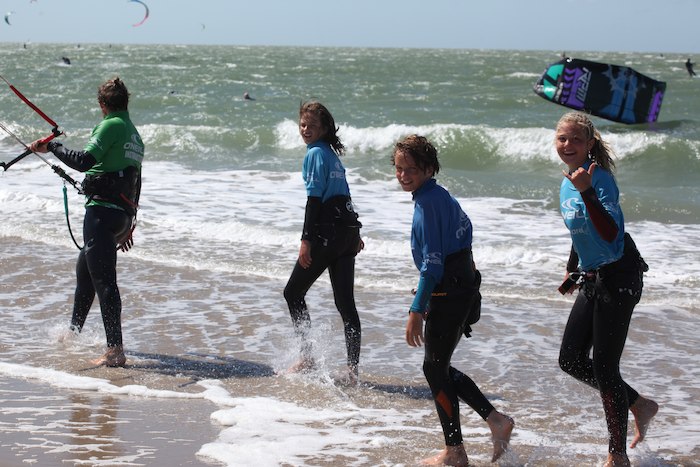 Kinder laufen im Kitesurfcamp in die Wellen und lächeln in die Kamera