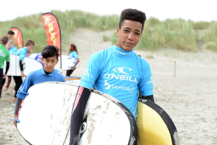 Jongen met surfboard loopt over het strand tijdens een surfkamp zomer